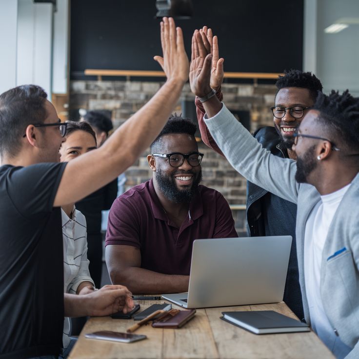 A team of builders celebrating with a high five over a laptop